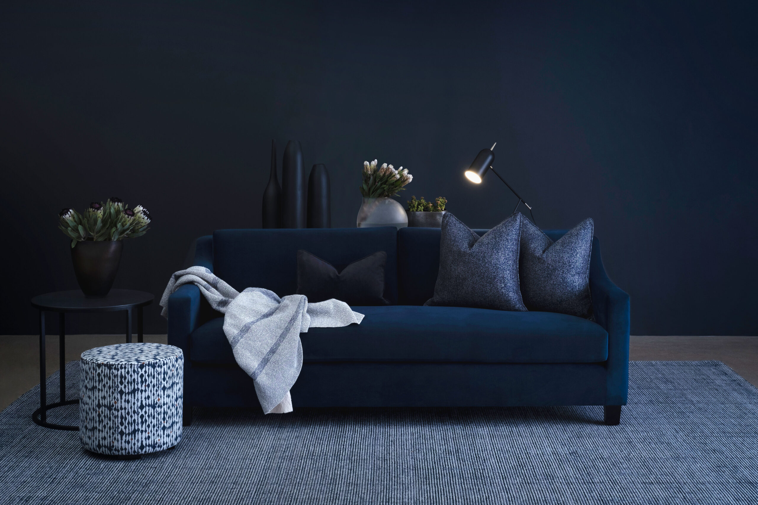 Dark blue sofa with grey rug and scatter cushions for high-end bachelor pads