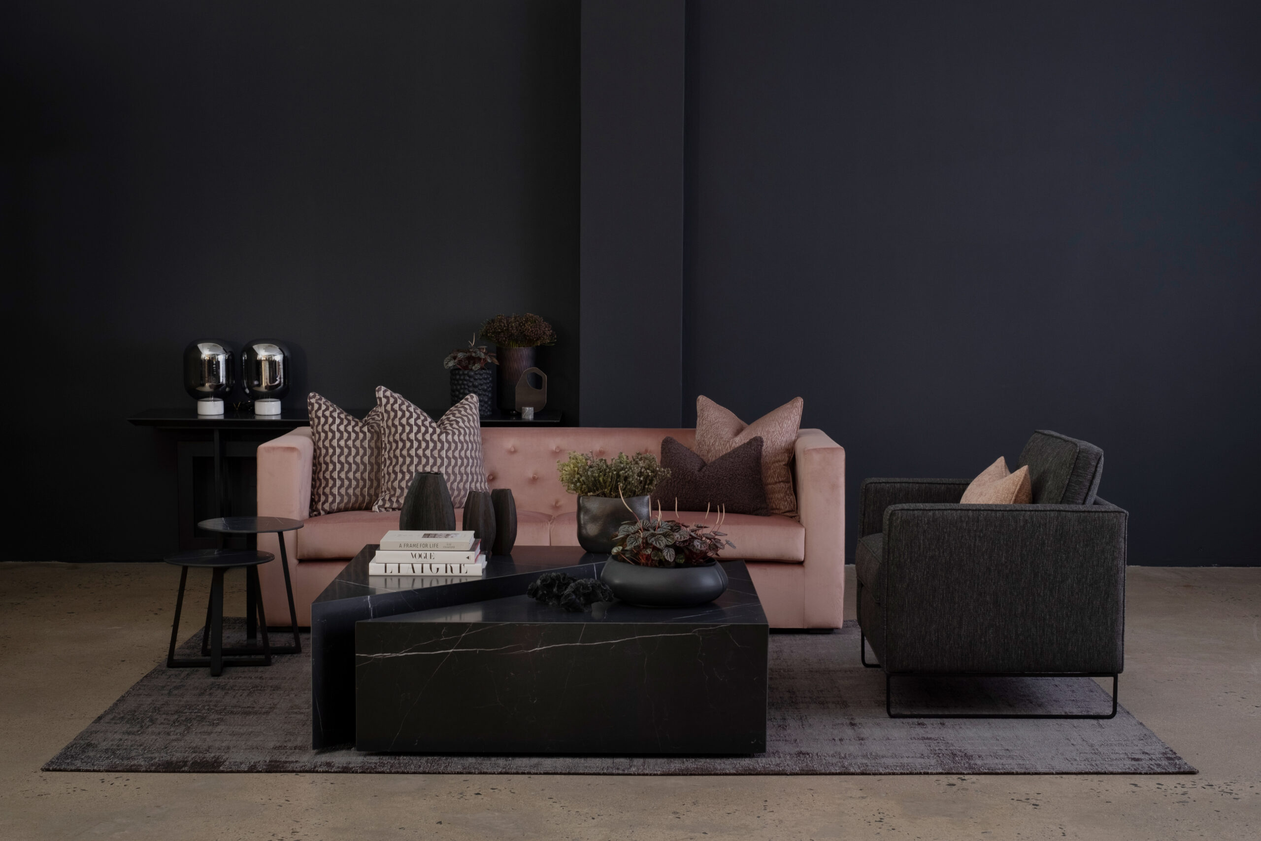 Lounge decor featuring pink three-seater and black one-seater couches with black marble coffee table and decorative vases and flowers