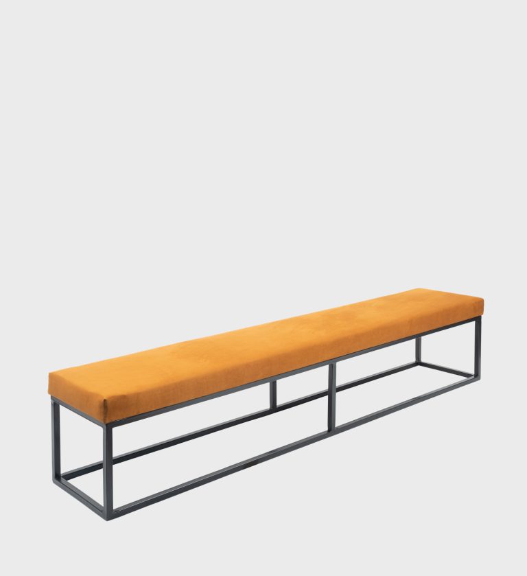 The Kelly Ottoman Flat Top embodies sleek modernism with its elongated silhouette and vibrant ochre upholstery.