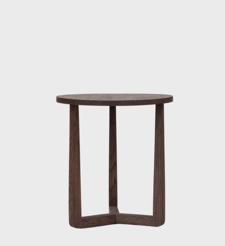 The Afton Side Table Large Walnut embodies timeless simplicity with a sculptural edge. Crafted from rich walnut wood, its circular top rests on three subtly tapered legs joined by a triangular base, creating a harmonious balance of form and stability