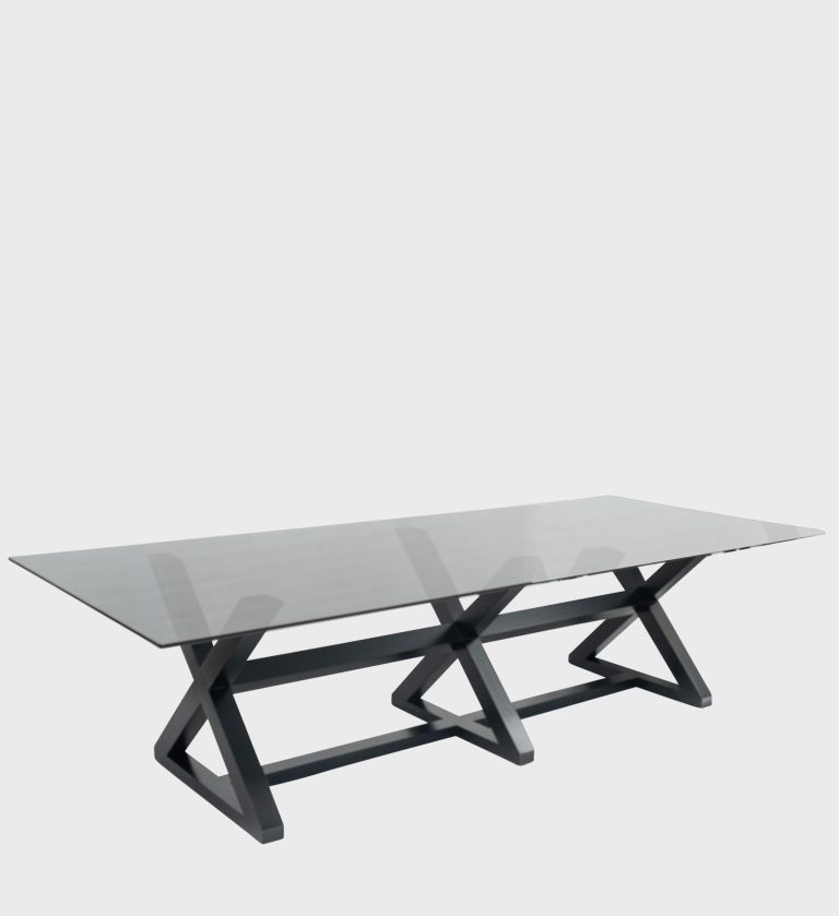 The Jam XXX Dining Table Smokey Glass Top is a striking blend of industrial precision and modern elegance. Its expansive rectangular glass top, tinted in a subtle smoky hue, rests on a bold geometric base composed of two interlocking X‑shaped frames