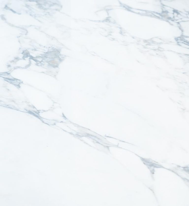 The Bellissima Table is a striking fusion of elegance and modern geometry. Its round marble‑effect top, with subtle gray veining, rests on a sculptural black base composed of angular intersecting legs.