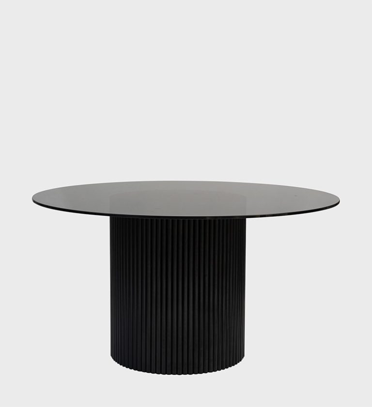 The Luvuvhu Round Dining Table is a refined statement of modern elegance. Its circular smoked‑glass top rests on a cylindrical base adorned with vertical fluting in deep black, creating a striking interplay of transparency and texture.