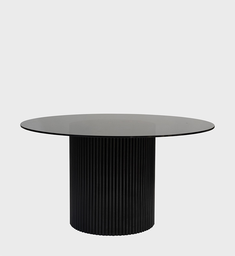 The Luvuvhu Round Dining Table is a refined statement of modern elegance. Its circular smoked‑glass top rests on a cylindrical base adorned with vertical fluting in deep black, creating a striking interplay of transparency and texture.