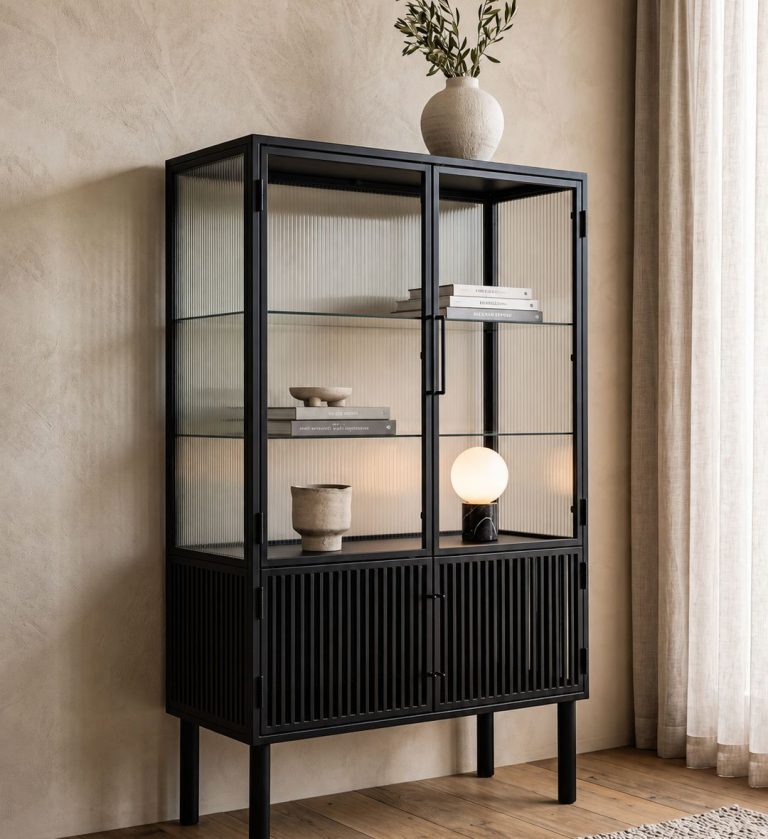 The Lauren Cabinet is a refined showcase of modern craftsmanship. Its tall, structured frame combines sleek black wood with vertically fluted glass panels, creating a dynamic interplay of light and shadow.