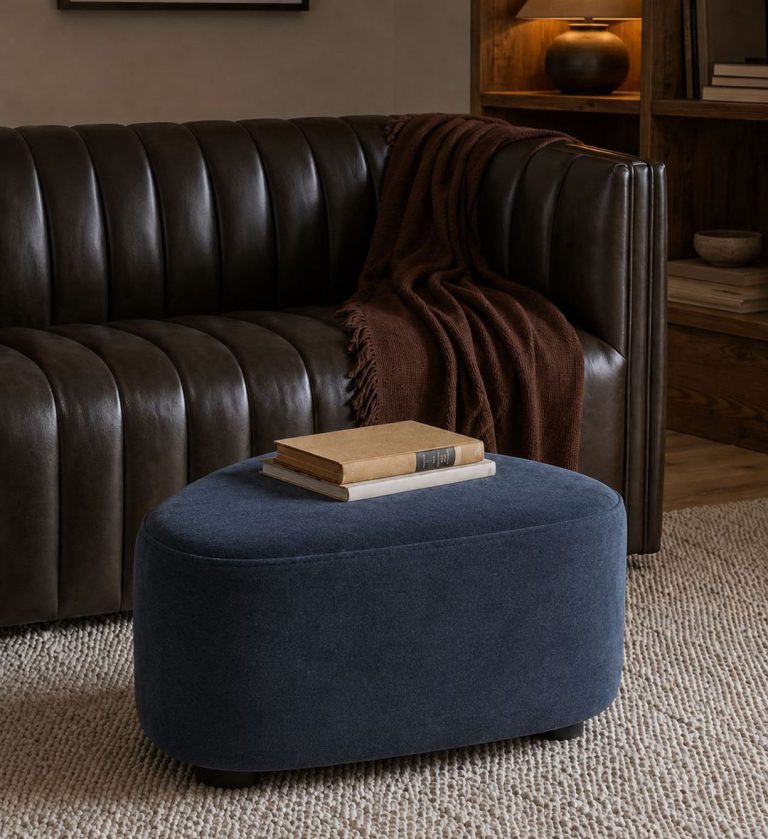 The Pebble Ottoman brings playful elegance to modern interiors with its organic, rounded triangular form and smooth navy upholstery.
