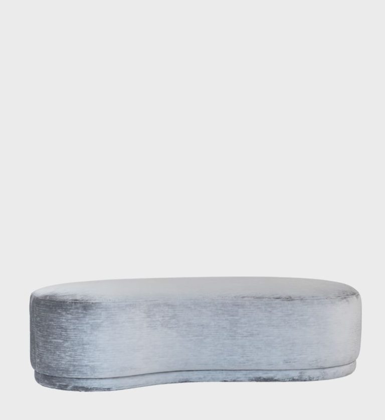 The Opal Ottoman exudes understated elegance with its fluid, curved silhouette and luxurious velvet upholstery in a soft silver tone.