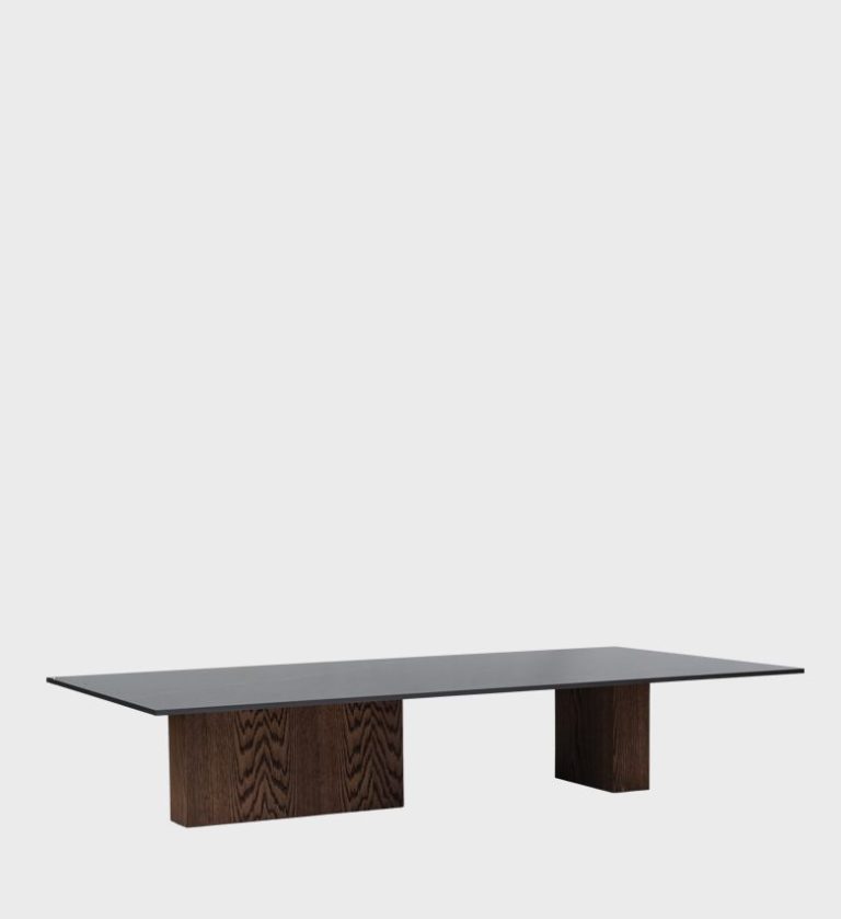 The Stratus Coffee Table embodies minimalist sophistication with architectural balance. Its expansive rectangular top, finished in a smooth dark surface, rests on two solid wooden block bases